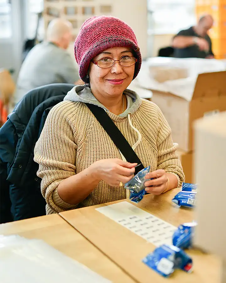 Frau mit Mütze arbeitet an einem Tisch und etikettiert Produkte.