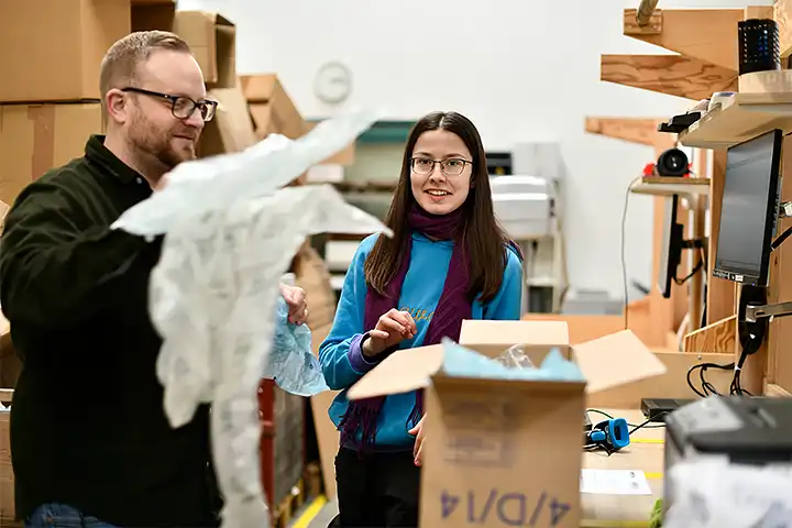 Mann macht ein Paket versandbereit, junge Frau hilft ihm dabei.
