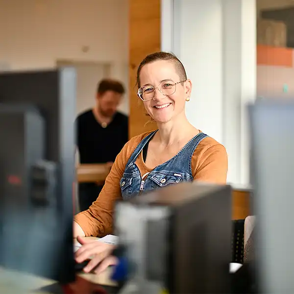 Frau mit kurzen Haaren arbeitet am PC und lächelt freundlich