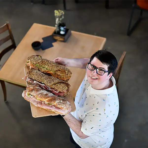 junge Frau mit kurzen Haaren serviert drei leckere Sandwich im CAFE SAM